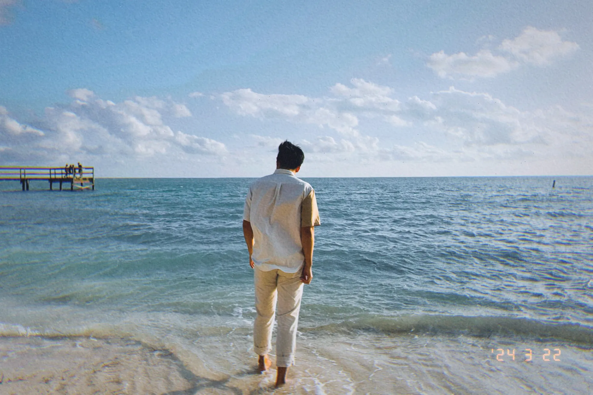 With his back to the camera, Daniel stands on the beach.